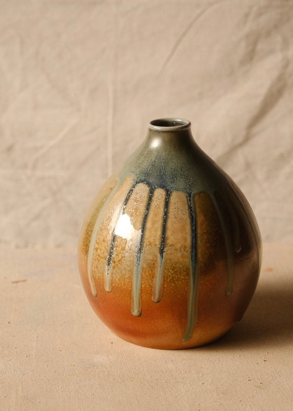 Woodfire Orbe Vase shown from the front, glaze drips streaming down its round orange-toned body against draped linen.