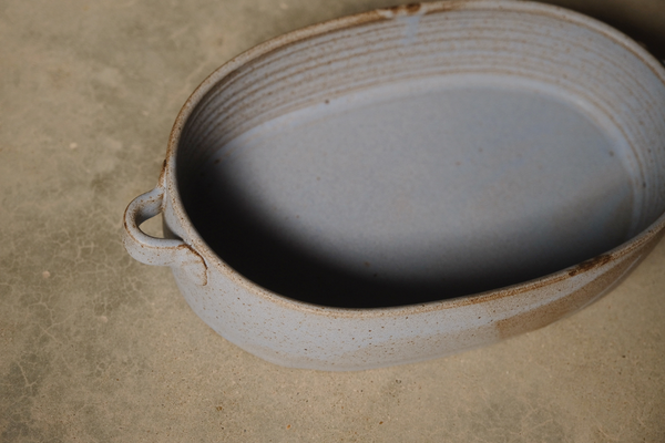Cenote Hot Dish, close-up angled view showing a speckled glazed oval baker with grooved interior walls and side handle.