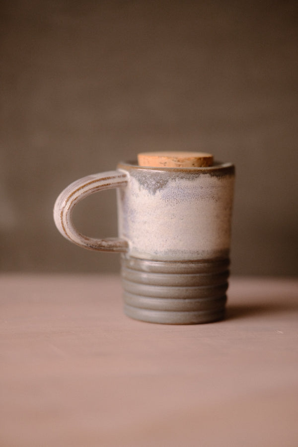 Stormy Sky Traveller travel mug with cork lid, handle on left. Pale grey top half, ridged grey bottom on a pale surface.
