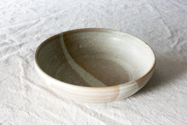 Wander Pasta Bowl in two-tone glaze with spiral interior, resting on crinkled linen fabric.