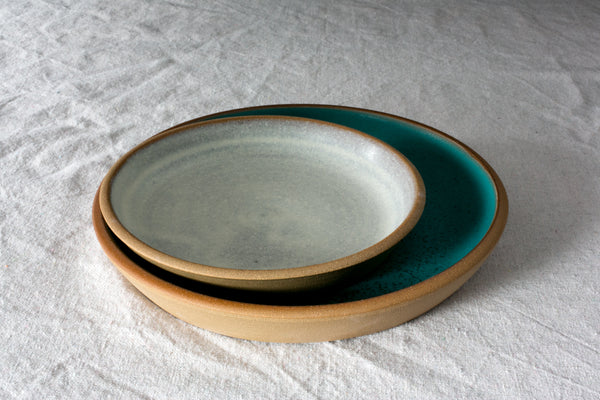 Fat Rim Lunch Plate in soft white nested inside a larger turquoise stoneware plate on textured linen